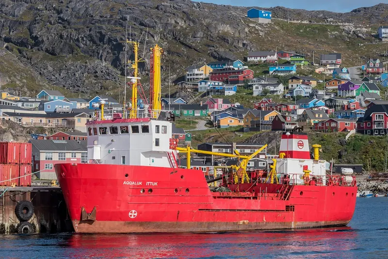 The Royal Arctic Line vessel Aqqaluk Ittuk at the dock in Qaqortoq, the colourfully painted houses of South Greenland's largest town rising up the hillside behind.