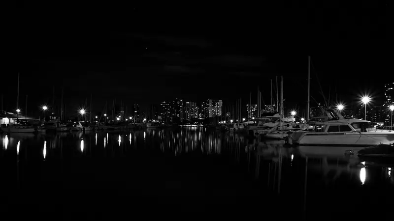 Ala Wai Harbor after dark, dock lights reflecting across still water with the Waikiki skyline behind.