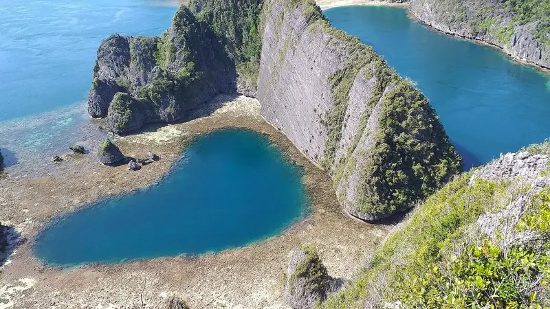 A deep lagoon sits enclosed by karst walls, its dark centre dropping away from a rim of bright reef flat.