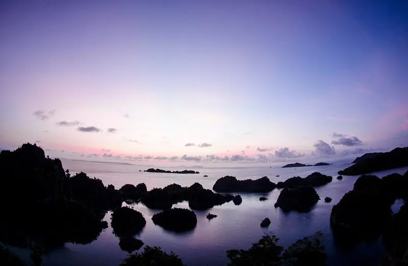 Dawn turns the sky pink over the islands, with boats lying anchored between them in flat water.