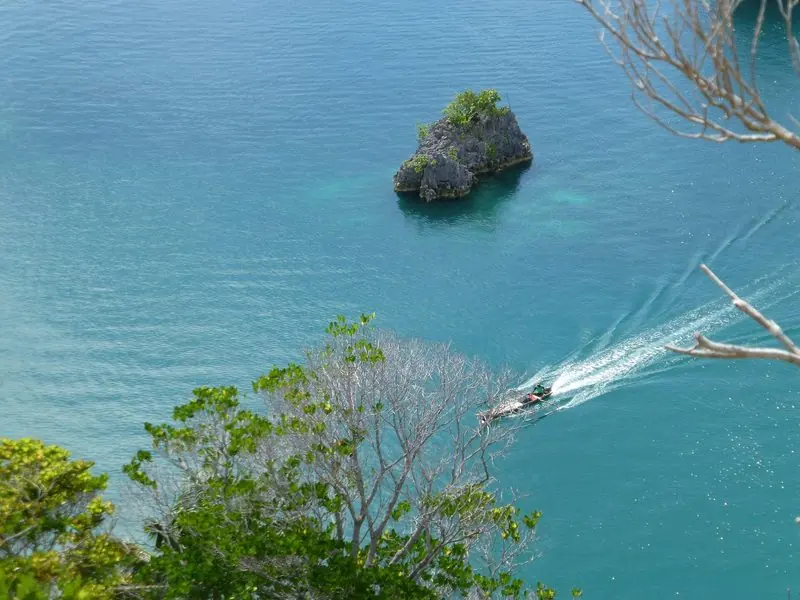 Below the ridge an outrigger crosses clear water past a single karst islet, its wake the only mark on the surface.