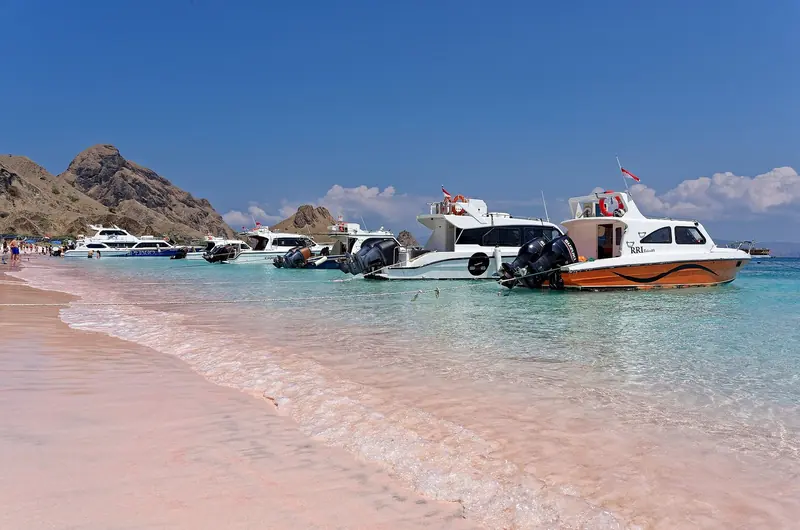 Speedboats and liveaboard tenders anchored off Pink Beach on Padar's east coast, the pink tint coming from crushed red foraminifera shell mixed into the white sand.