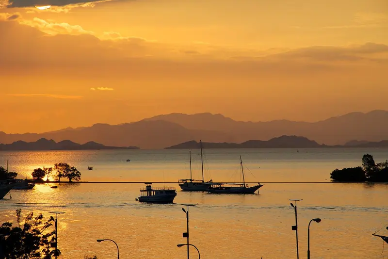Traditional phinisi-rigged liveaboards at anchor off Labuan Bajo at sunset, the gateway port for every Komodo charter.
