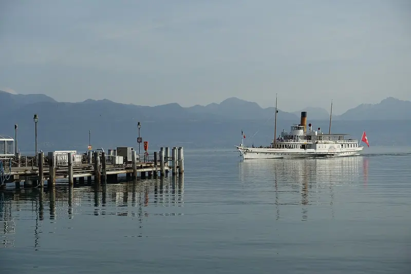 A CGN paddle steamer sits at its pier off Lausanne, the French Alps rising hazy across the water behind it.