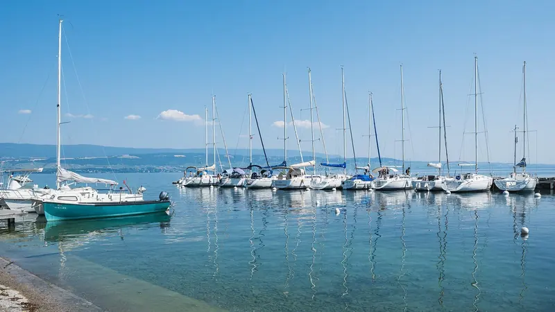 Sailing boats lie moored in the small harbour at Yvoire, on the lake's southern, French shore, the water flat and clear.