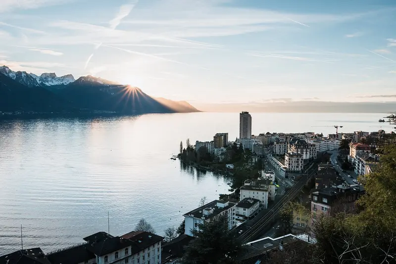 Montreux catches the last of the sun over Lake Geneva, the town's waterfront and towers reflected in still water.
