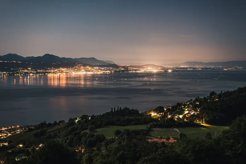 Evian-les-Bains lights up the French shore after dark, seen across the water from the Lavaux vineyard terraces above Lausanne.