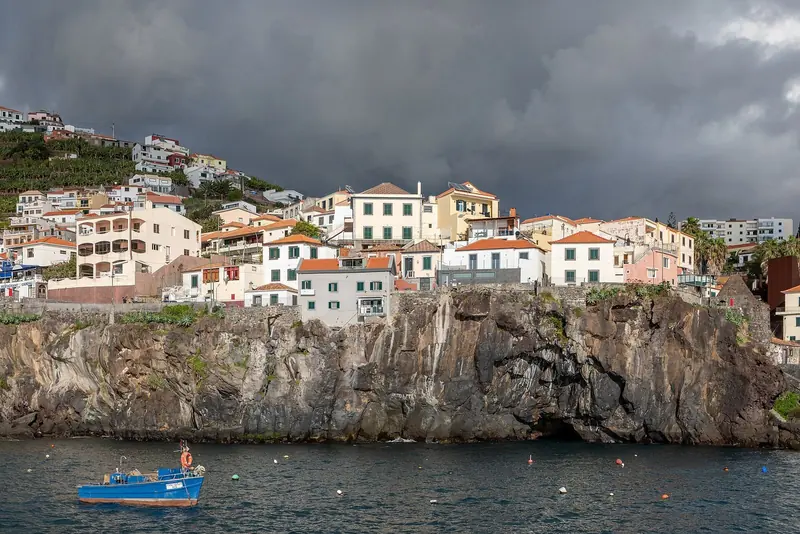 Camara de Lobos, the fishing village Winston Churchill painted, stacked on its cliff above a small boat riding its mooring in the bay.