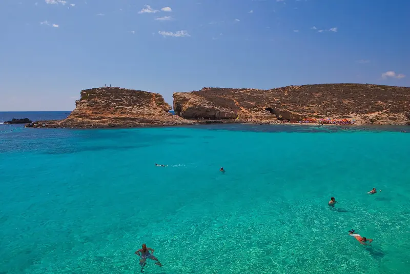 Swimmers in the shallows off Comino, where a marked swimming zone covers the lagoon in summer and boats may not cross the buoys.