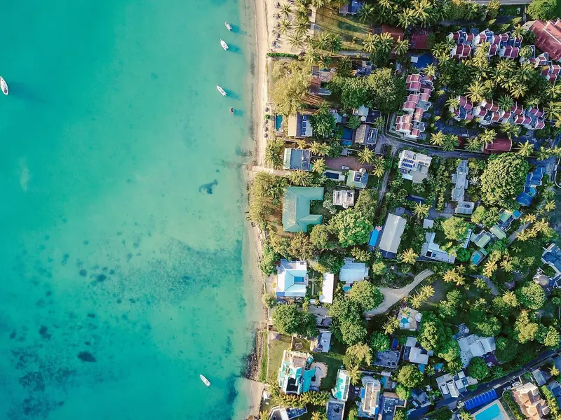 Aerial view of the Grand Baie shoreline, villas and pools backing directly onto the turquoise lagoon with small boats moored just offshore.