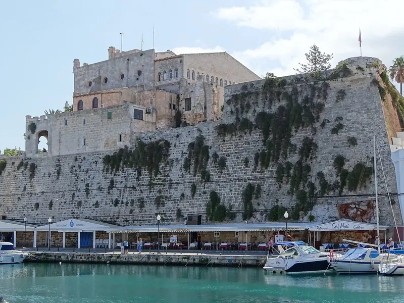 The bastion wall of Ciutadella's old citadel drops straight into the harbour, with the quayside restaurants and visitor berths at its foot.