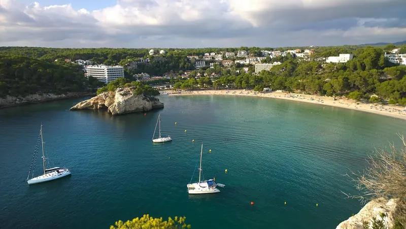 Cala Galdana on a summer afternoon, yellow mooring buoys marking the regulated field where anchoring on the bay's seagrass is not permitted.