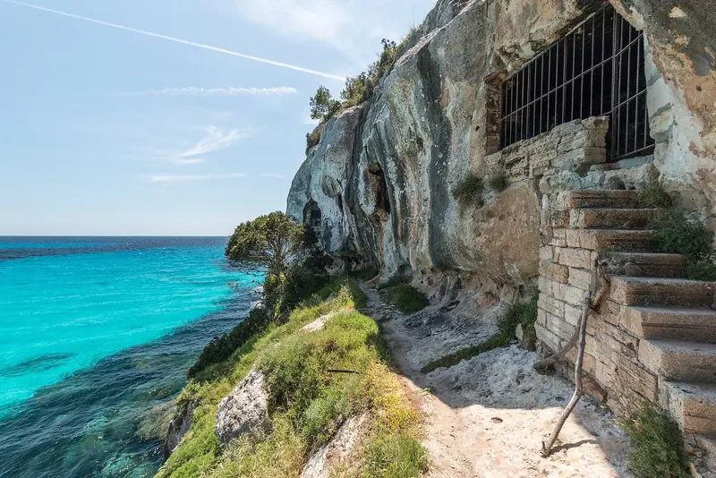 The man-made caves cut into the limestone above Cala Macarella, with the marine reserve's clear water below.