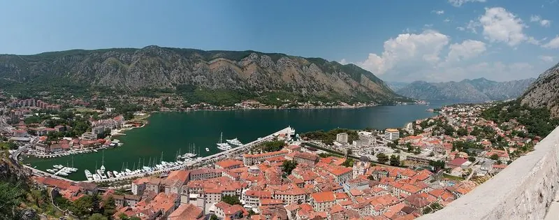 Perast runs along the north shore of the Bay of Kotor, stone houses dropping to a working quay with the morning cloud still hanging on the ridge behind.
