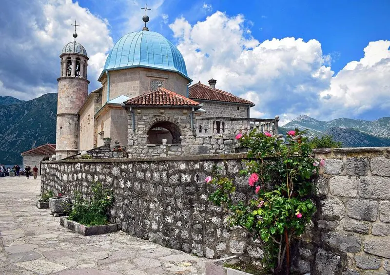 Roses grow along the low wall of the island, where a paved terrace runs right around the church and the mountains close in on every side.