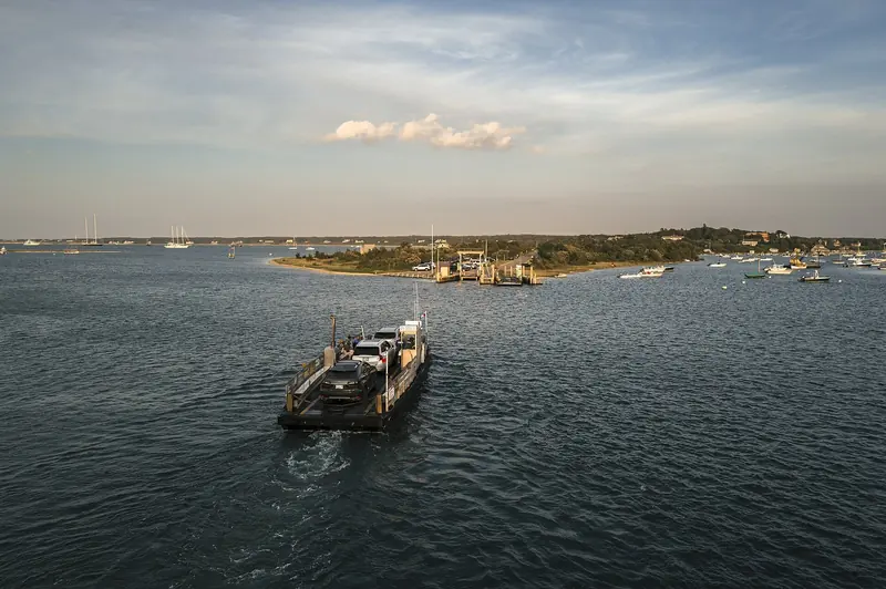 The Chappaquiddick ferry crosses to Edgartown, Martha's Vineyard, with boats moored in the harbor beyond.