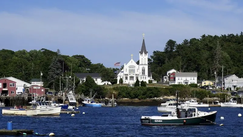 Lobster boats ride their moorings off Boothbay Harbor, the white church and the bait wharves close along the shore.