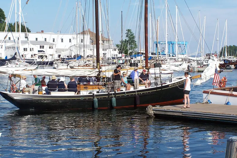 Passengers board a Camden windjammer at the town dock, her masts crowded in among the yachts and the harbourfront hotel behind.