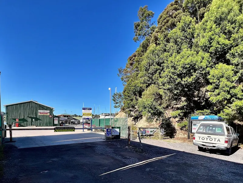 The working gate at Opua's boatyard - travel-lift signage, a security barrier and masts stacked behind the fence, the unglamorous end of the marina that actually hauls and services the fleet.