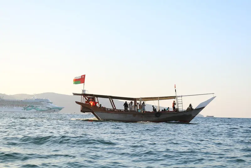 A dhow under way with the Omani flag, the working craft of a coast where the fishing villages in the khors have no road to them.
