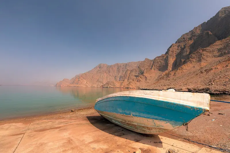 A boat hauled out on the shingle below red mountains, the whole of the shore side infrastructure in most of Musandam.
