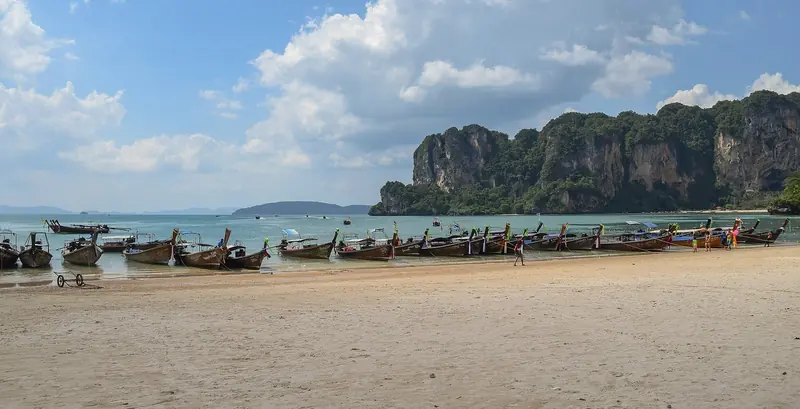 Longtail boats on the sand at Railay under the overhanging limestone, reached from the water rather than by road.