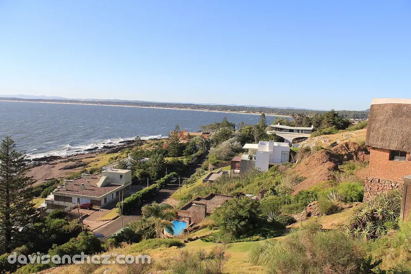 The coast toward Punta del Este seen from Punta Ballena, with the thatched eave of a Casapueblo building at the right of the frame.