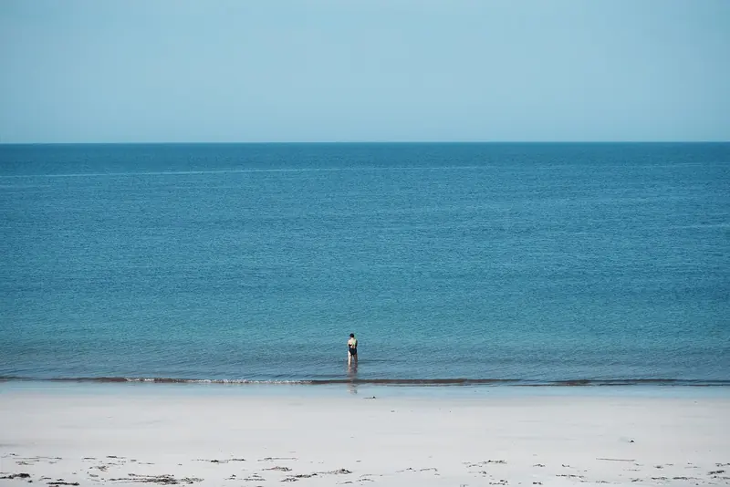A Hebridean beach of white shell sand with a single figure on it, the water clear, empty and about thirteen degrees in August.