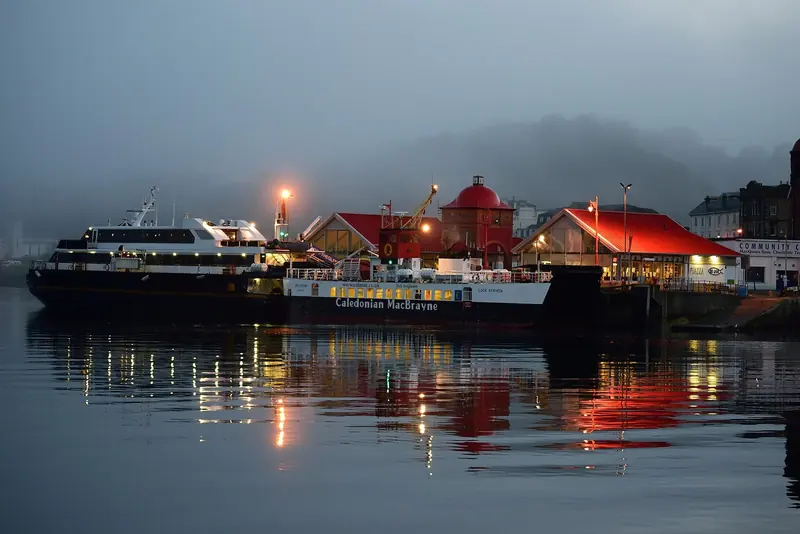 Oban waterfront at dusk in the mist, the mainland town that supplies the whole west coast and sits three miles from its only large berth.