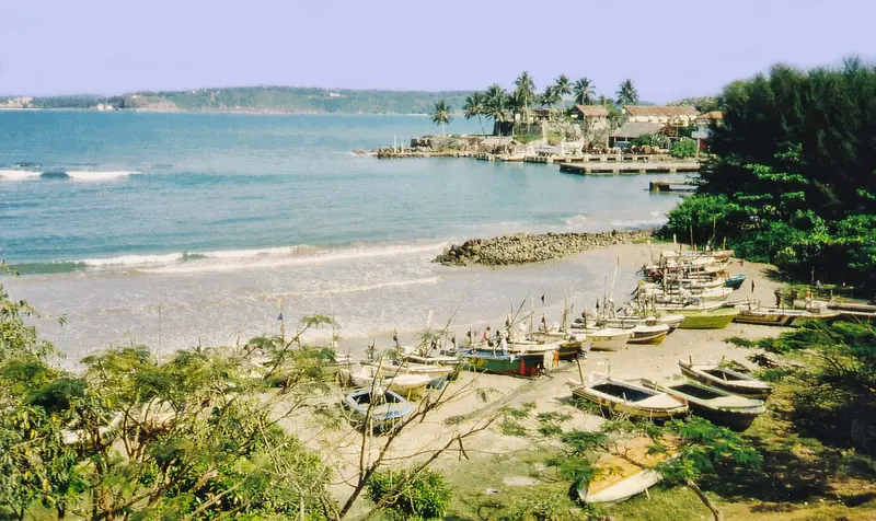 Fishing boats hauled up on the sand inside Galle's outer bay, with the old harbour and its breakwater beyond, the sheltered water a visiting yacht shares with the town's working fleet.