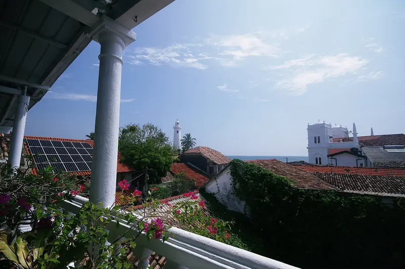 The lighthouse and red-tiled roofs of Galle Fort seen from a colonial-era veranda, the view that greets crews once they clear the harbour gate on foot.