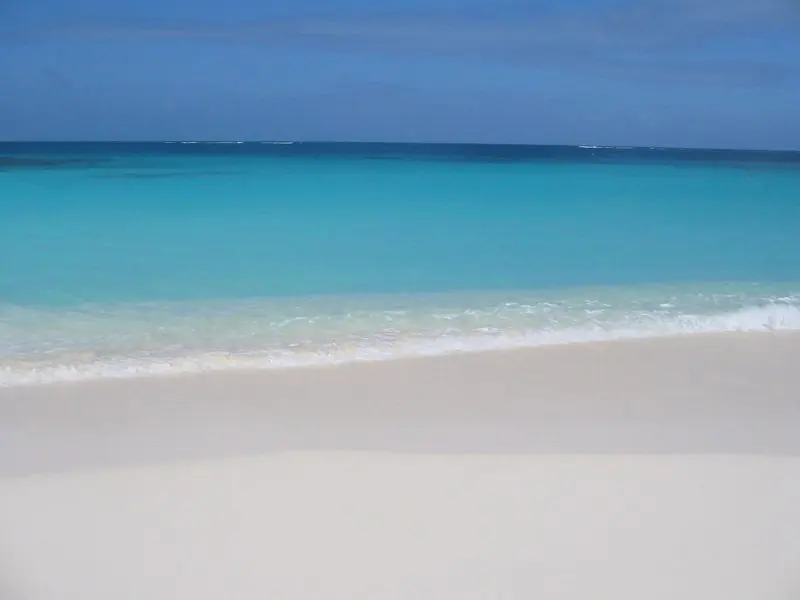 Shoal Bay on Anguilla shelves off white sand into clear turquoise, with the reef line breaking white along the horizon.