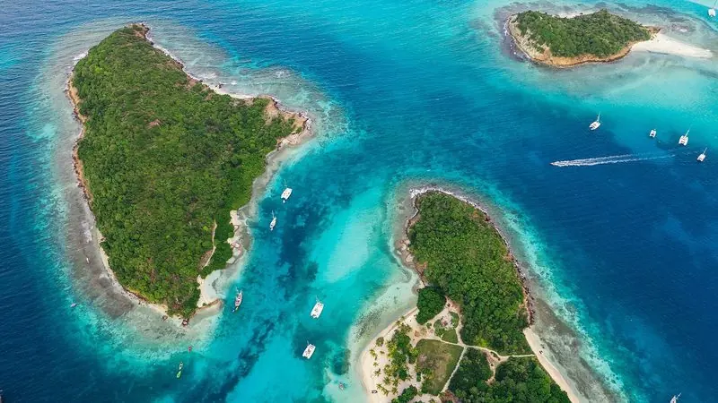 Tobago Cays sit low and uninhabited inside the horseshoe reef, catamarans anchored on clear sand with the swell breaking well outside them.