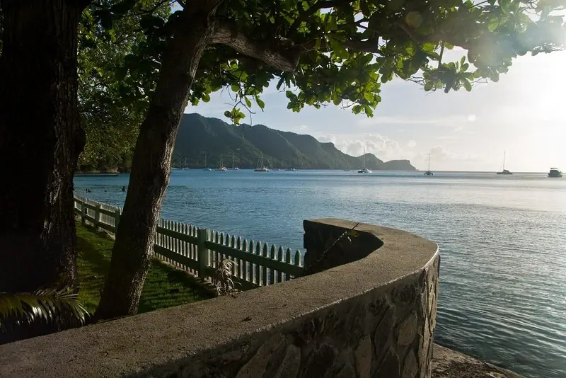 A low seawall and picket fence carry the shoreside walk along the Bequia waterfront, the anchored fleet spread across the bay behind it.