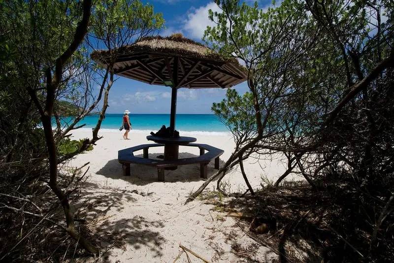 Scrub opens onto the white sand and hard blue water of Macaroni Beach on Mustique, where a thatched table is the only structure in sight.