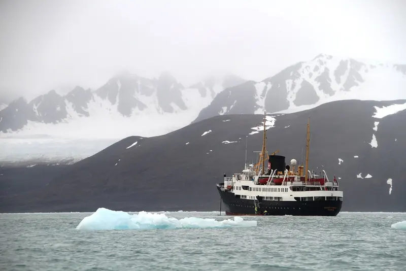 An expedition ship at anchor in a fjord with ice in the water, at the scale the 200 passenger limit in protected areas produces.