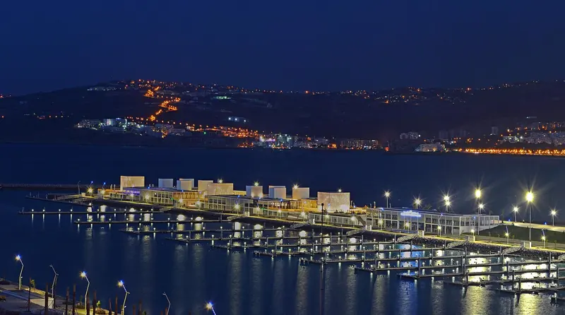 Tanja Marina Bay after dark, its pontoons built into the old harbour basin at the foot of the medina, with the hills of the bay behind it.