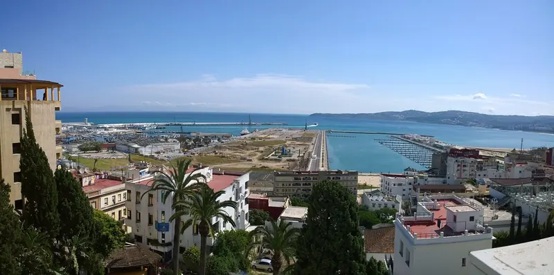 Tangier's hillside city and harbour seen from above, with the causeway and breakwater that shelter the port reaching out into the bay.
