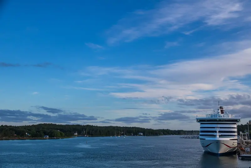 A Baltic cruiseferry docked at Mariehamn at dusk, with sailboats anchored in the bay beyond, Aland Islands.