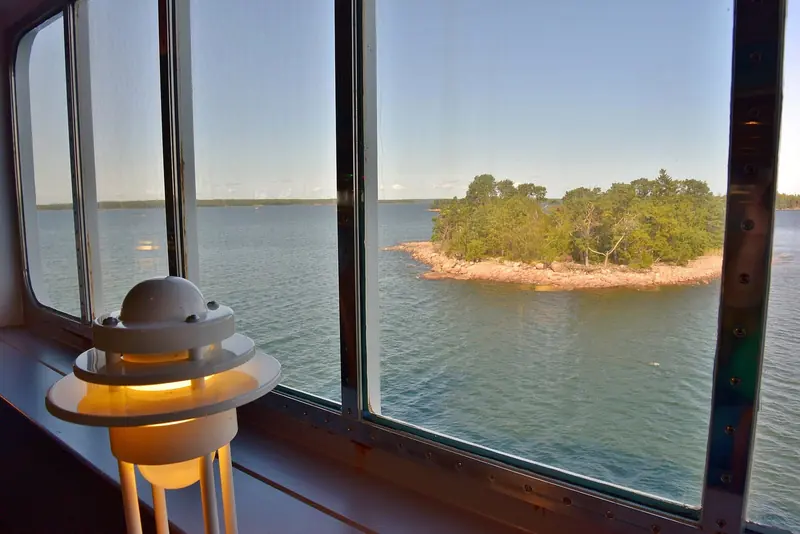 A granite skerry island fringed with pine trees, seen from a ferry crossing the Aland Islands archipelago.