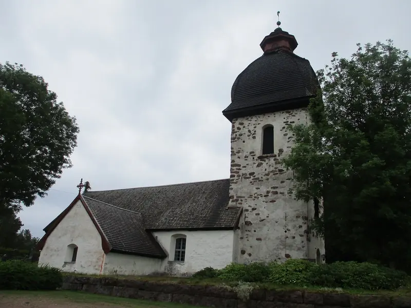 A whitewashed medieval stone church with a dark bell tower, one of the parish churches scattered across the Aland Islands' farming villages.