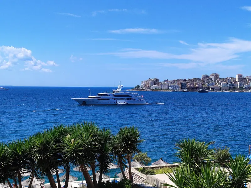 A charter yacht anchored off Saranda, with the town's waterfront apartment blocks behind it.