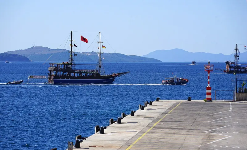 Excursion boats leaving Saranda harbour, with Corfu's hills visible across the strait in the background.