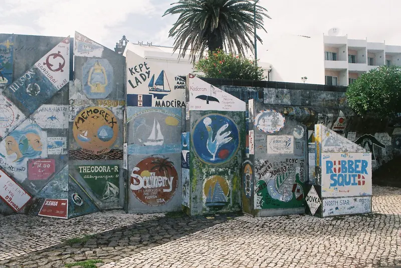 Boat names and crests painted on the Horta marina wall, a tradition sailors treat as compulsory