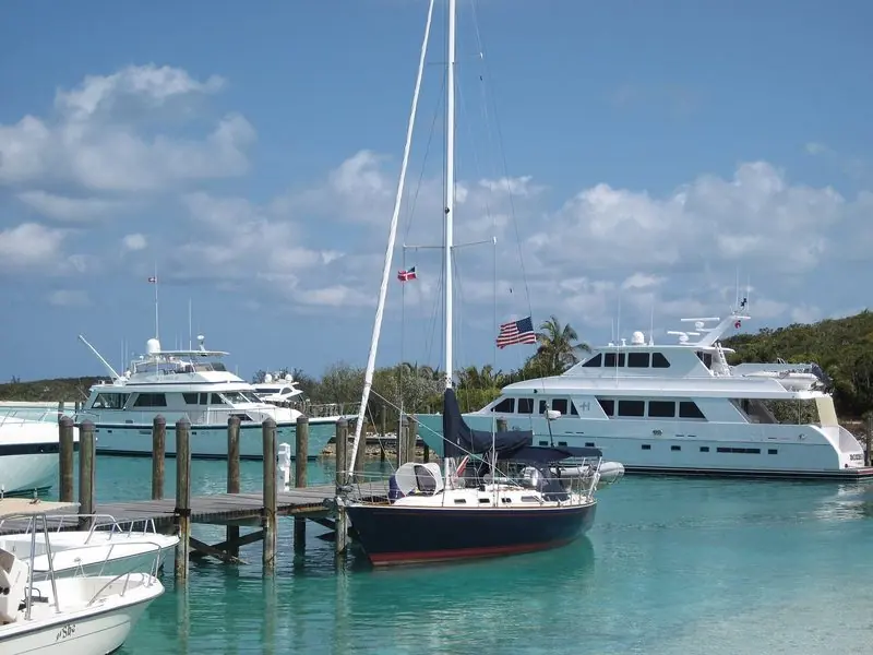 A ketch motors through pale turquoise shallows between two low green cays.