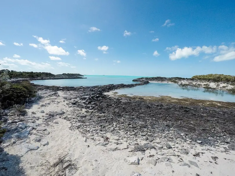 Limestone ironshore drops into a shallow mangrove pool with the bank running out to turquoise beyond. Ground like this is why so much of the chain is unusable to a deep keel and why the shallow-draft boats get the anchorages.