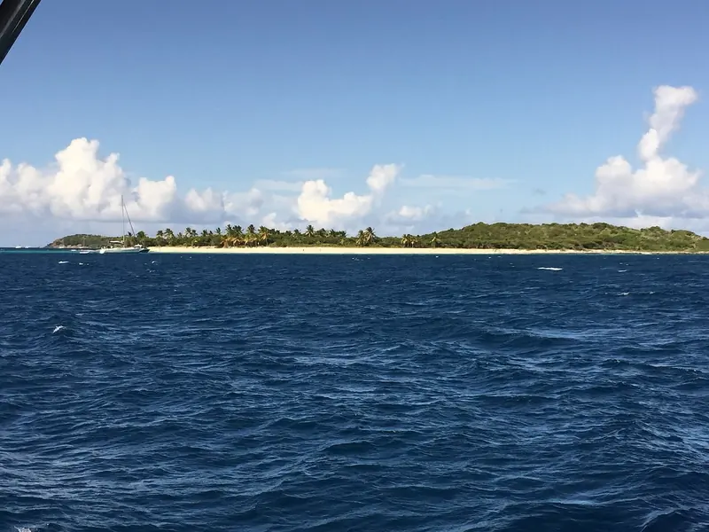 Anegada seen across the channel, a coral atoll so low that the palms show before the land does, ringed by 18 miles of reef.