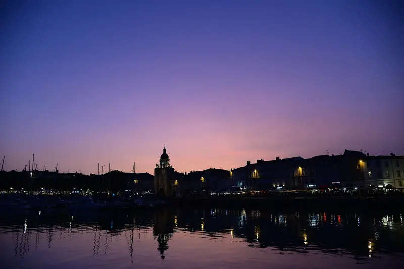 La Rochelle's old harbour glows at dusk, the clock tower and waterfront houses catching the last purple light over still water.