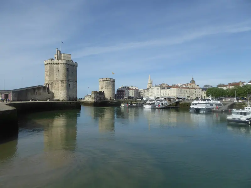 The Tour Saint-Nicolas and Tour de la Chaine flank the entrance to La Rochelle's Vieux Port, boats moored quietly between them.