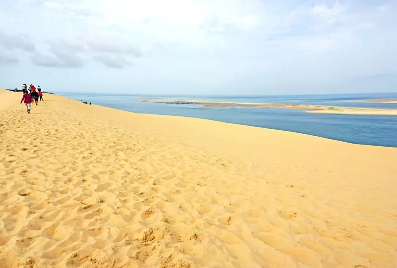 Walkers descend the Dune du Pilat's steep face toward Arcachon Bay, dwarfed by the scale of the sand underfoot.
